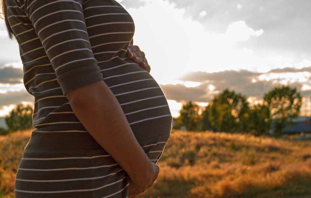 Pregnant Woman Standing in Field at Sunset